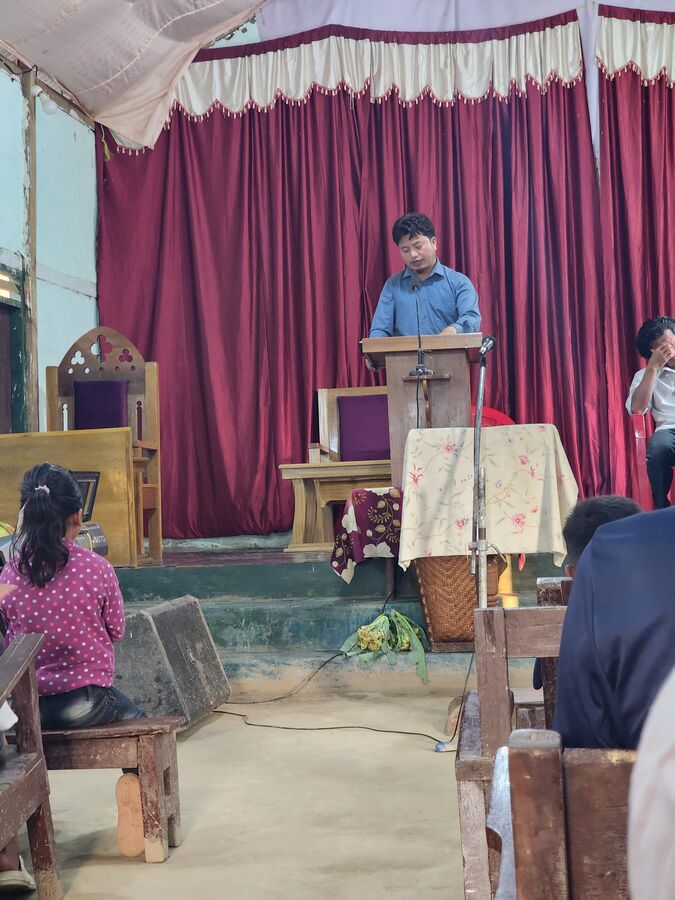 A woman teaching from a lectern in a small church.